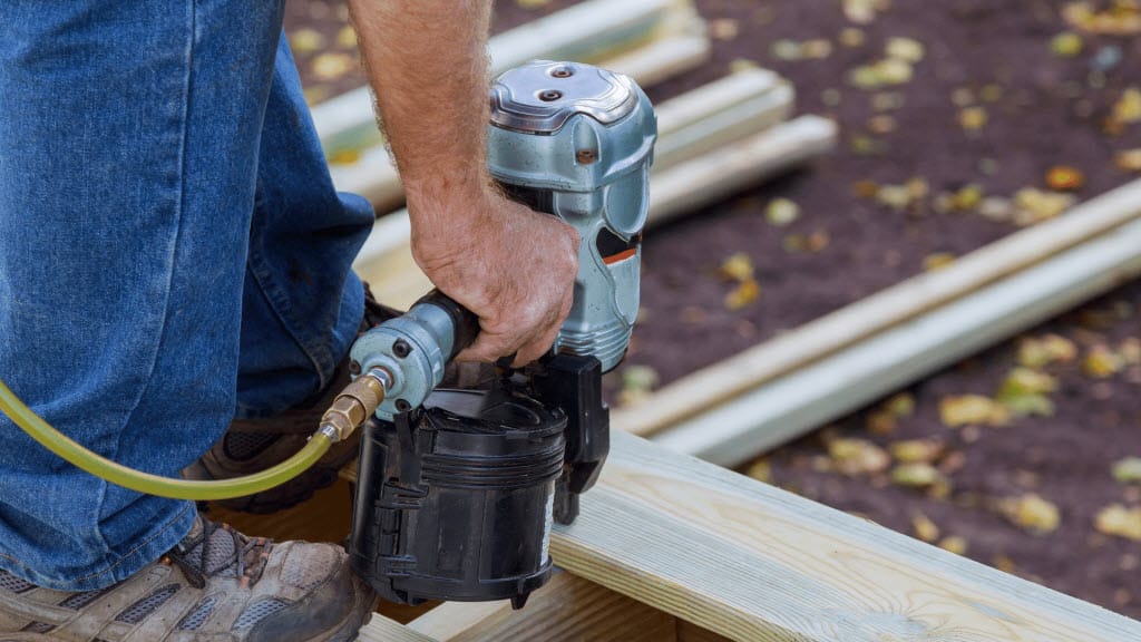 Worker using a nail gun to install timber decking boards
