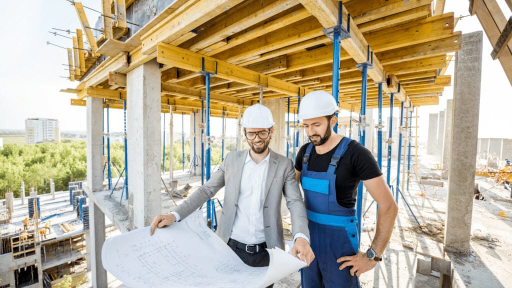 Two builders in hard hats reviewing building plans on a construction site